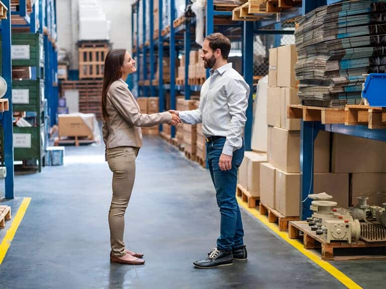 Photo de 2 adultes qui se serrent la main dans un entrepôt logisitque